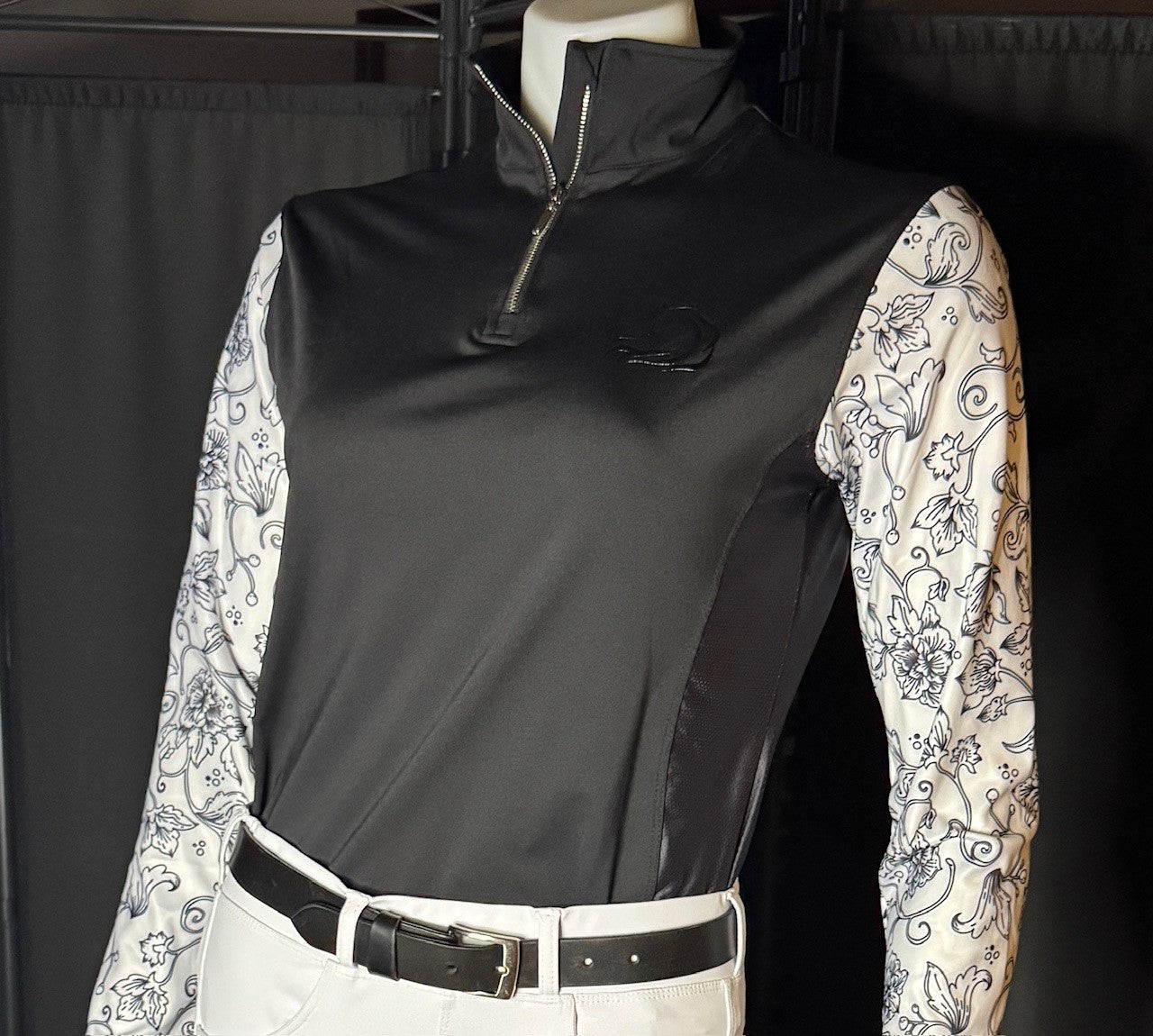 Women's black Midnight Floral Quarter-Zip riding shirt, intricate white floral sleeves, breathable mesh panels under arms, moisture-wicking fabric, and quarter-zip closure for equestrian comfort and style by PK Equine